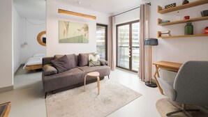 A modern living room with a grey sofa, a small wooden stool, a floor lamp, and a desk with shelves. - Tolkiena Charming Apartment (Warszawa)