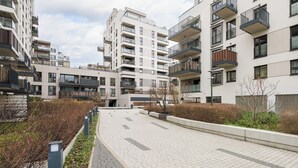 A modern apartment complex with multiple balconies, a paved walkway, and a landscaped area with shrubs. - Tolkiena Charming Apartment (Warszawa)