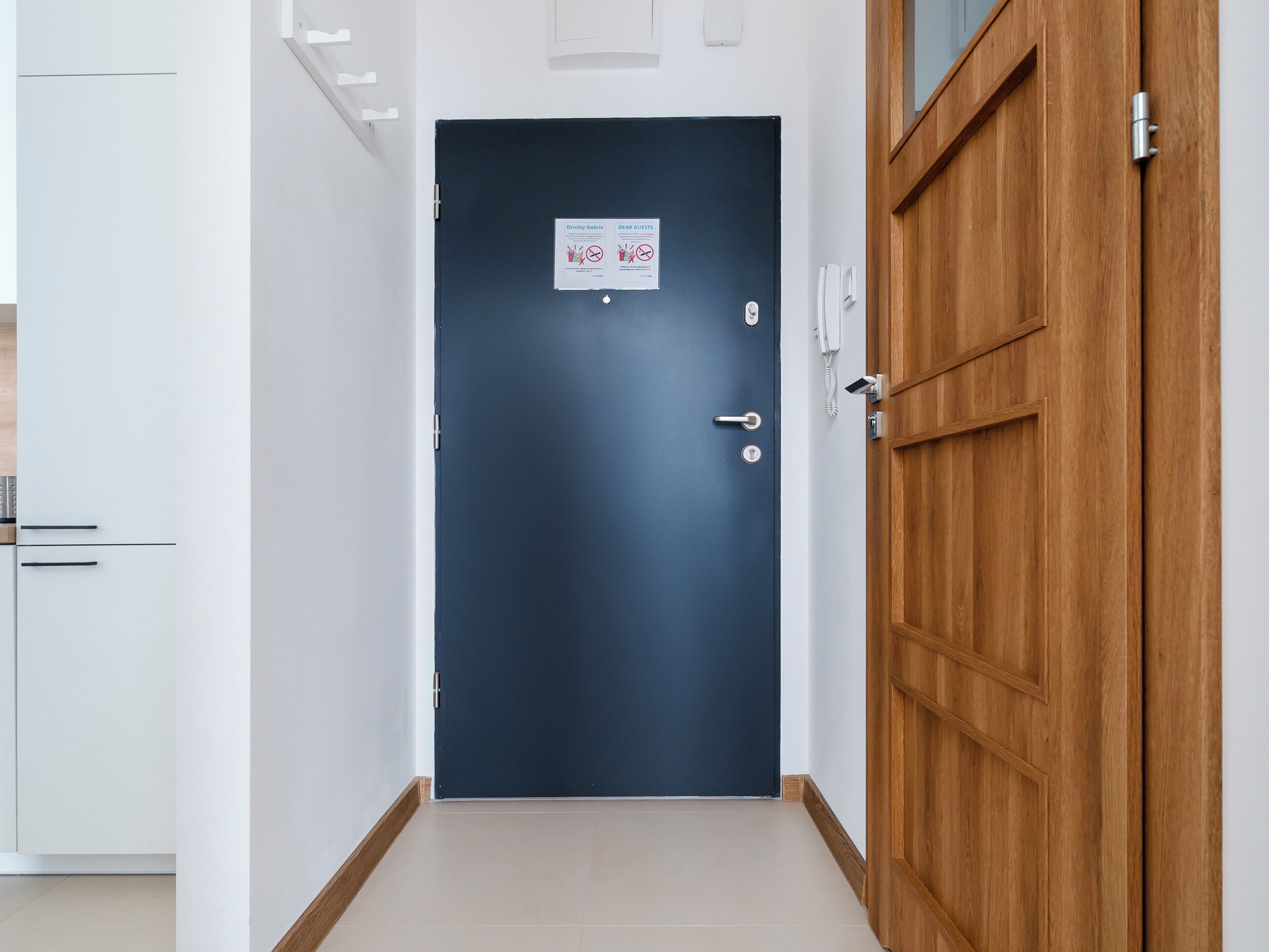 A blue door with a sign, a wooden door, and a white wall with a phone and a light switch.