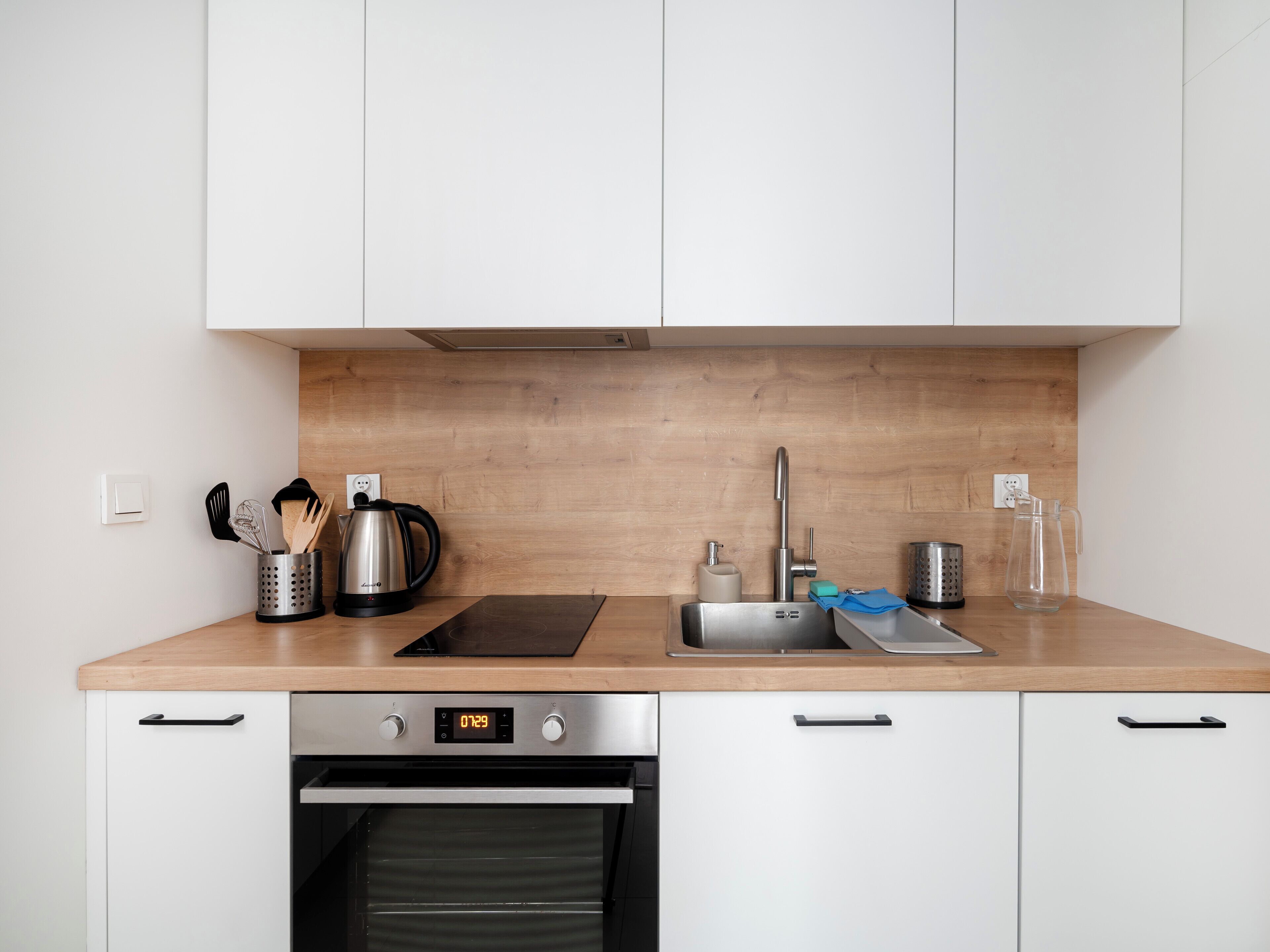A modern kitchen with white cabinets, a wooden countertop, a stainless steel kettle, a coffee maker, a sink, and a dishwasher.