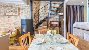 A dining area with a checkered tablecloth, wooden chairs, a fireplace, a stone wall, and a spiral staircase. - Holiday Home 'L'étable 15kms Puy Du Fou' with Private Terrace and Wi-Fi (Pouzauges)