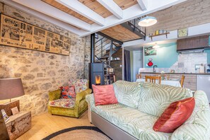 Ein gemütliches Wohnzimmer mit einer Couch, einem gemusterten Sessel, einer rustikalen Kommode und einer Steinwand.