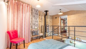 A room with a bed, a red chair, a bookshelf, a staircase, and a view of the outside. - Holiday Home 'L'étable 15kms Puy Du Fou' with Private Terrace and Wi-Fi (Pouzauges)