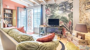 A living room with a sofa, television, and a wall with a tropical leaf pattern. - Holiday Home 'L' étable 15kms Puy Du Fou' with Private Terrace and Wi-Fi (Pouzauges)