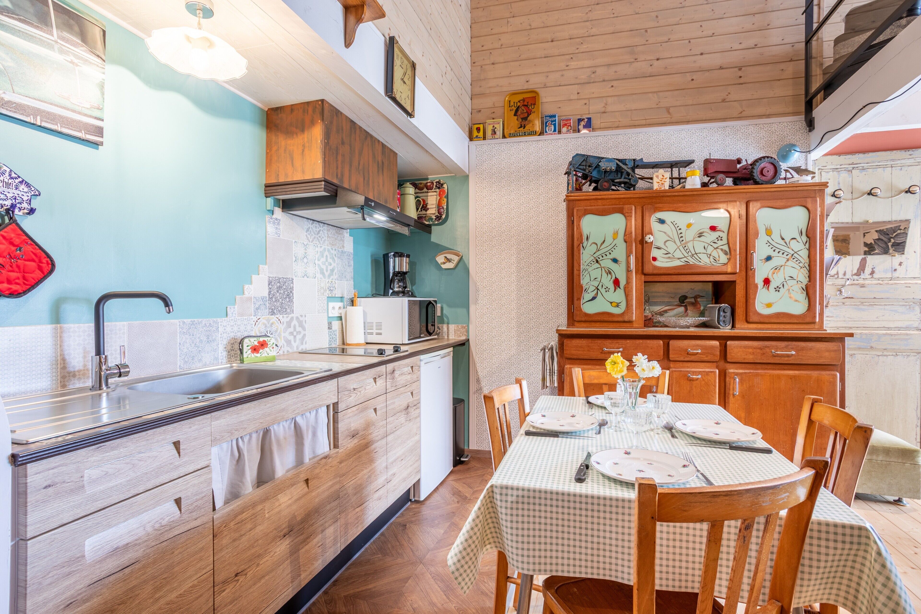 A kitchen with wooden cabinets, a dining table set for two, and a small refrigerator.