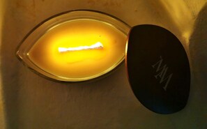 Una vela encendida dentro de un recipiente de vidrio con tapa que tiene un logo.