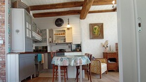 A compact kitchen with wooden beams, a dining table with chairs, and a small side table with a vase.