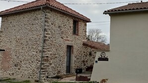 A stone building with a tiled roof, a door, and a small sign.