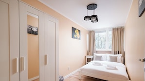 A bedroom with a bed, a nightstand, a window with curtains, and a ceiling light fixture.