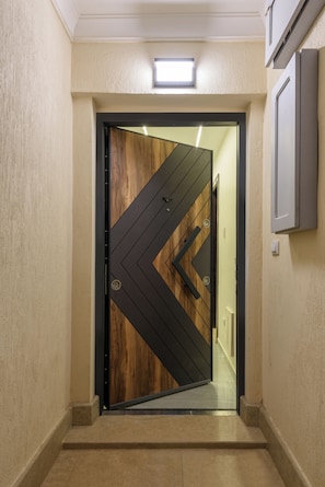 Corredor de interiores moderno com design geométrico único na porta, luminária acima da porta e escada visível que leva a outro nível.