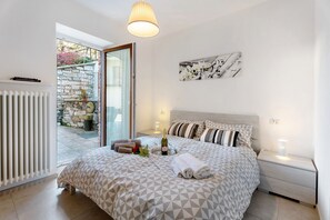 A bedroom with a bed, a nightstand, a bottle of wine, and towels. - Holiday Home 'Residenza Jasmine Grey Apartment' with Private Garden and Wi-Fi (Verbania)