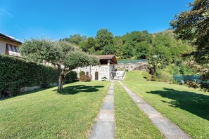 Un bâtiment en pierre avec un toit rouge, un chemin de pierre menant à l’entrée et un jardin luxuriant et verdoyant.