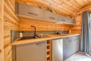 A compact kitchen with wooden walls, a stainless steel sink, and grey cabinets.