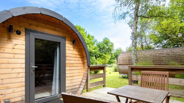 A wooden cabin with a curved roof, a sliding glass door, a deck, and a table with chairs. - Ôtonneauxstress – Beach Attendant: Unique Experience Just Steps from the Atlantic (Saint-Vivien-de-Médoc)