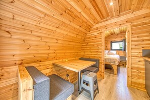 A wooden cabin interior with a bed, a table, and a bench.