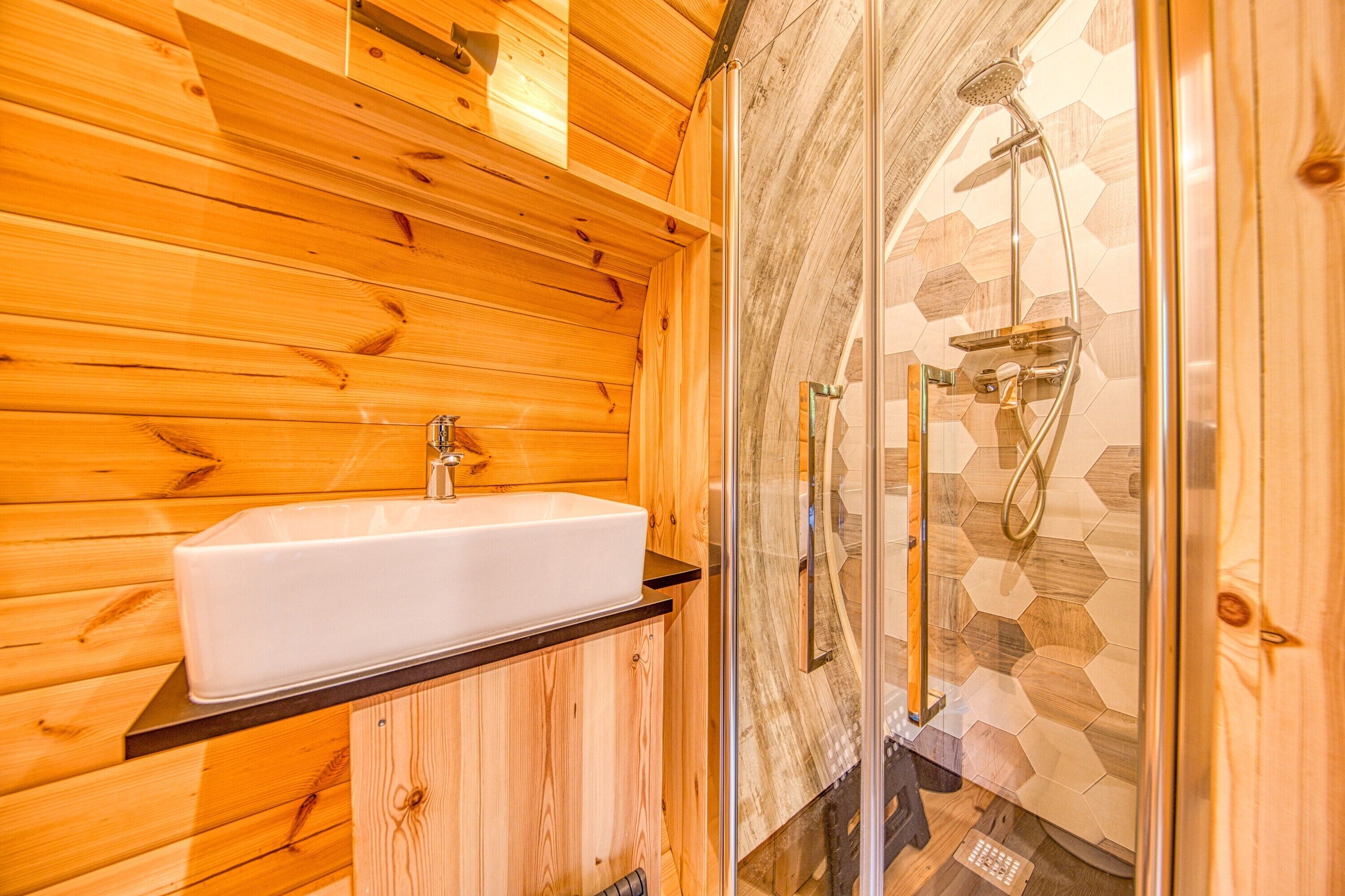 Een houten blokhut vanbinnen, met een witte wastafel, houten kastjes en een douche met een glazen deur.