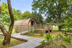 A small wooden cabin with a covered porch, surrounded by trees and a grassy area. - Ôtonneauxstress – Le Pêcheur: Relaxation and Nature in the Médoc, Close to the Ocean (Saint-Vivien-de-Médoc)