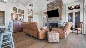 A spacious living room with leather sofas, a stone fireplace, and a flat-screen TV. - The Cajun Cottage - Private Boat Launch/Dock (Ocean Springs)