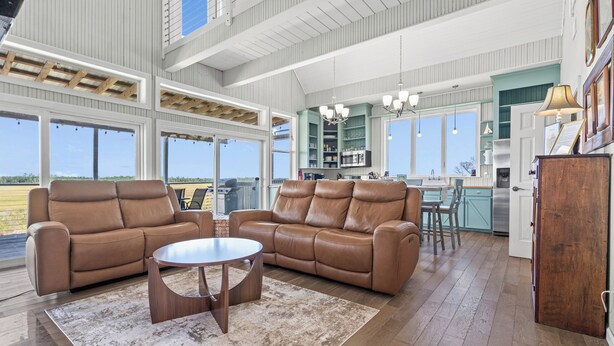A spacious living area with a large brown leather sofa, a round coffee table, and a view of the outdoors. - The Cajun Cottage - Private Boat Launch/Dock (Ocean Springs)