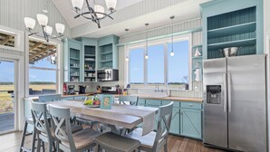A modern kitchen with a dining area, featuring a large island, stainless steel appliances, and light blue cabinetry. - The Cajun Cottage - Private Boat Launch/Dock (Ocean Springs)