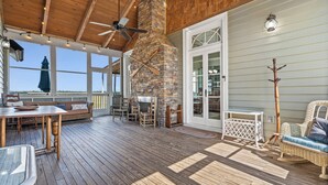 A covered deck with a stone fireplace, wooden furniture, and large windows. - The Cajun Cottage - Private Boat Launch/Dock (Ocean Springs)