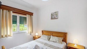 A bedroom with a bed, two bedside tables with lamps, a window with curtains, and a wall-mounted picture. - Room 'Quarto 4 - Jorge Galinheiro' with Mountain View, Shared Garden and Wi-Fi (Mamouros)