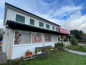 Un bâtiment blanc avec un auvent rouge, une enseigne et une vitrine où sont exposés des produits alimentaires.