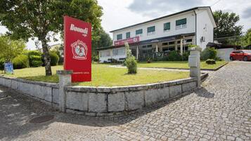 A building with a signboard, a paved area, and a red car parked nearby.