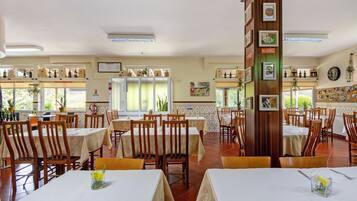 Un restaurant amb diverses taules i cadires, un piló alt amb quadres emmarcades, i vista cap a l'exterior.