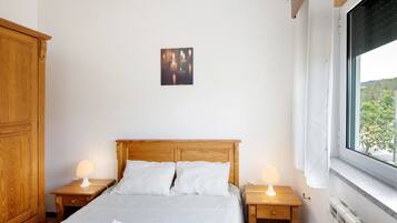 A bedroom with a wooden bed, two bedside tables with lamps, a radiator, and a window with a view.