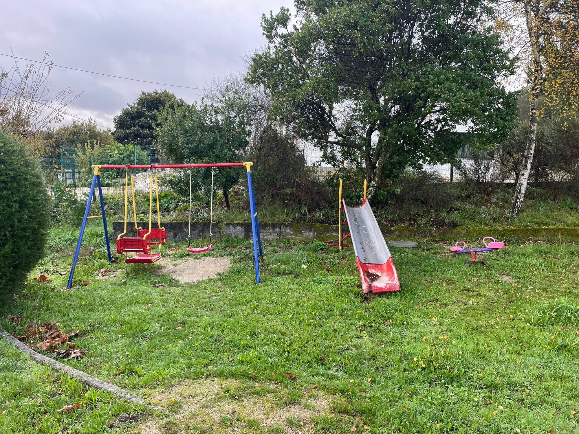 A playground with swings and a slide, surrounded by grass and trees.