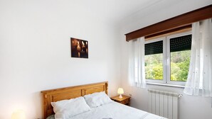 A neatly made bed with white linens, a bedside lamp, a radiator, and a window with curtains. - Room 'Quarto 5 - Jorge Galinheiro' with Mountain View, Shared Garden and Wi-Fi (Mamouros)