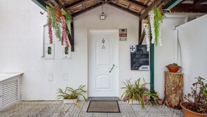 A white door with a doormat, hanging plants, and a signboard. - Room 'Quarto 5 - Jorge Galinheiro' with Mountain View, Shared Garden and Wi-Fi (Mamouros)
