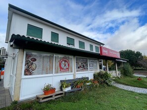 Ein weißes Gebäude mit roter Markise, einem Schild und einem Schaufenster voller Speisen.