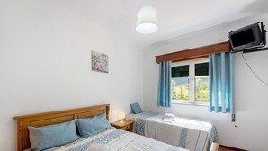 A bedroom with two beds, a TV mounted on the wall, and a window with curtains.