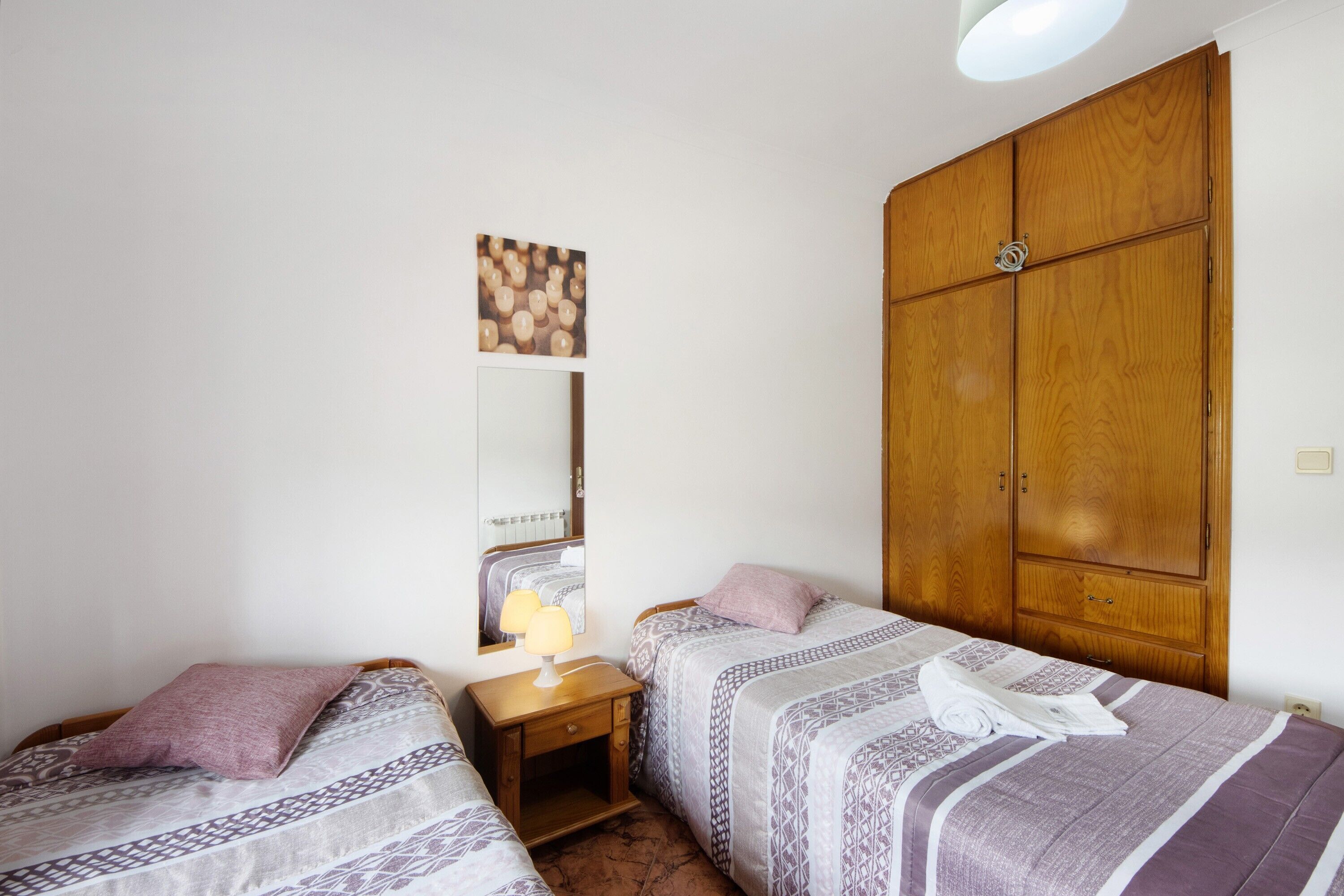 Une chambre avec deux lits, une armoire, un miroir et une table de chevet avec une lampe.