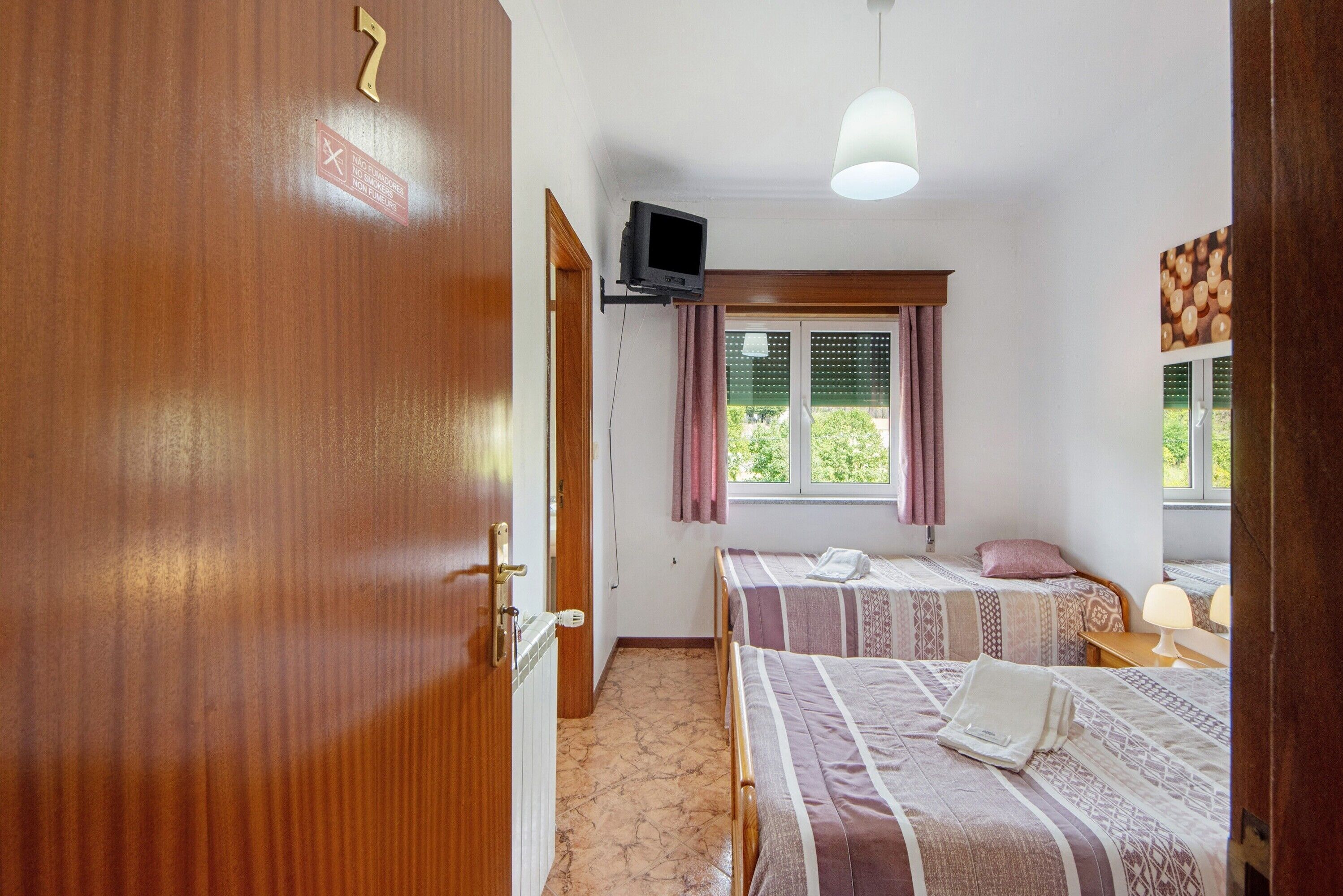 Ein Hotelzimmer mit zwei Betten, einem Fernseher, einem Fenster mit Vorhängen und einer Tür.