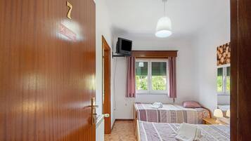 Ein Hotelzimmer mit zwei Betten, einem Fernseher, einem Fenster mit Vorhängen und einer Tür.