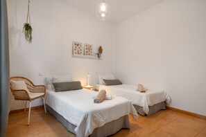 Ein Schlafzimmer mit zwei Betten, einem Sessel, einer hängenden Pflanze und Wandbildern.