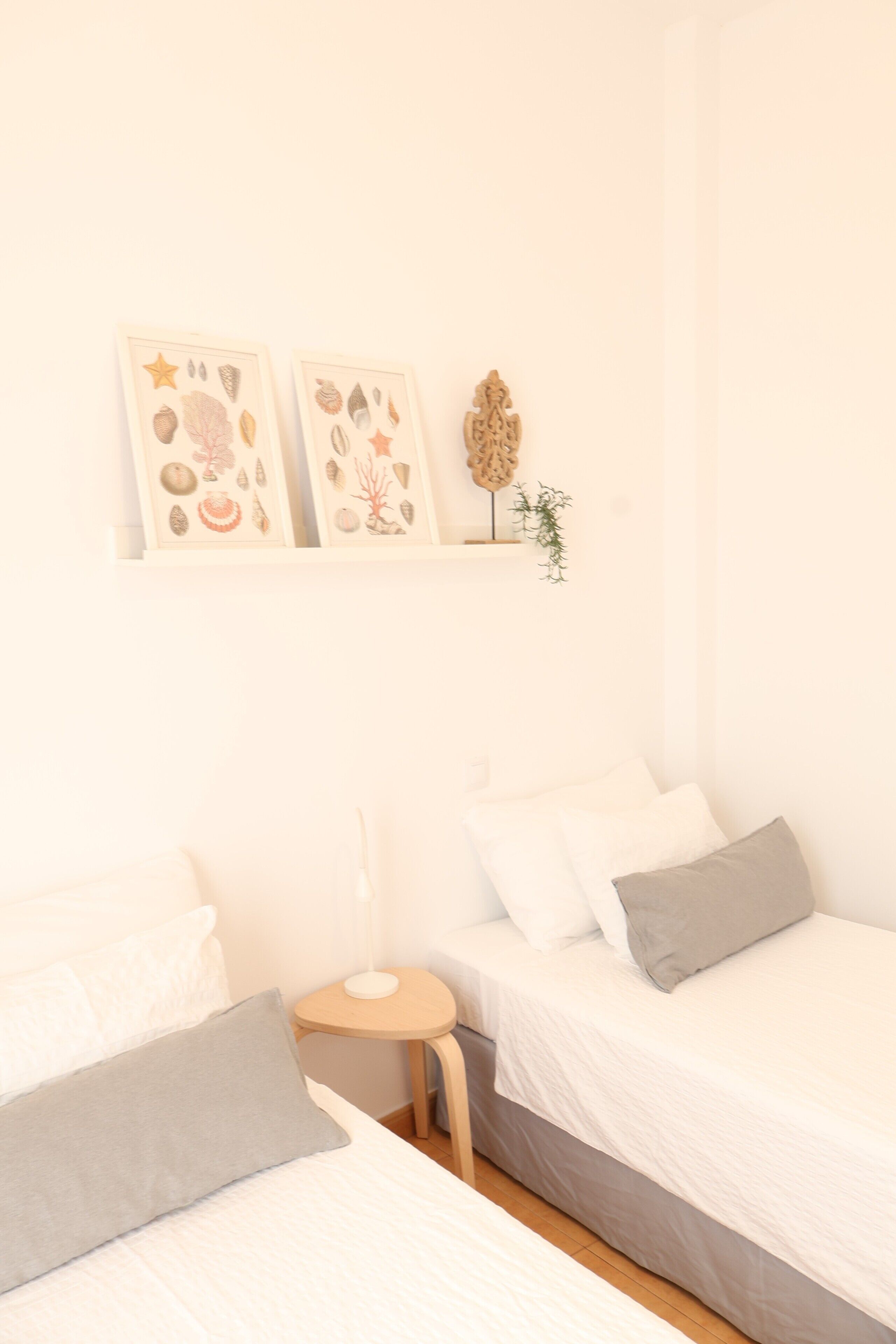 A bedroom with two beds, a small bedside table, and wall-mounted shelves with decorative items.