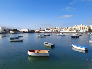 A marina with several boats docked, calm water, and buildings in the background.