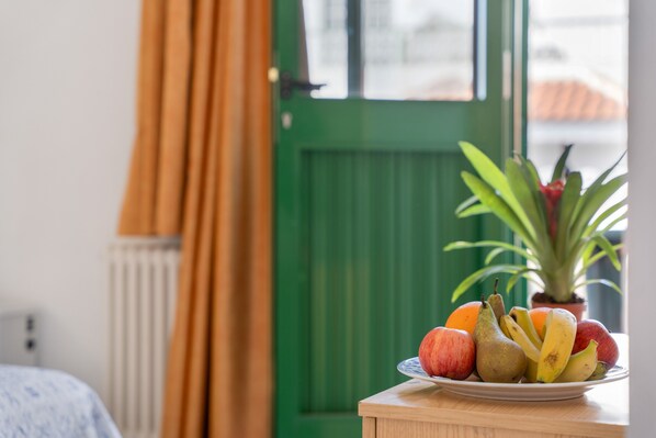 A fruit bowl on a table with a green door and curtains in the background.