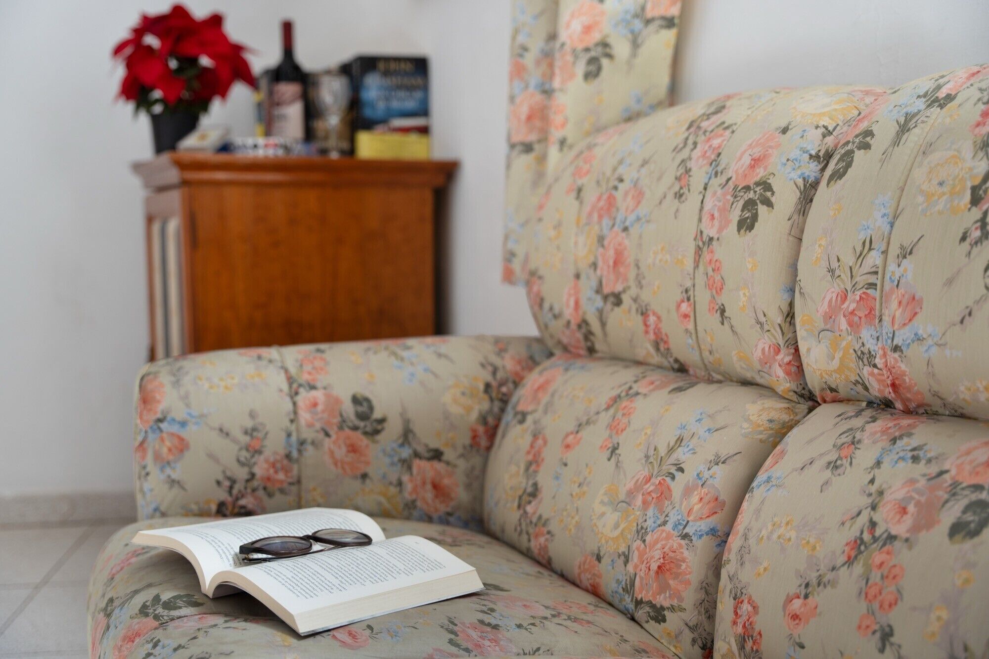 A sofa with a floral pattern, a book, and a pair of glasses on it.