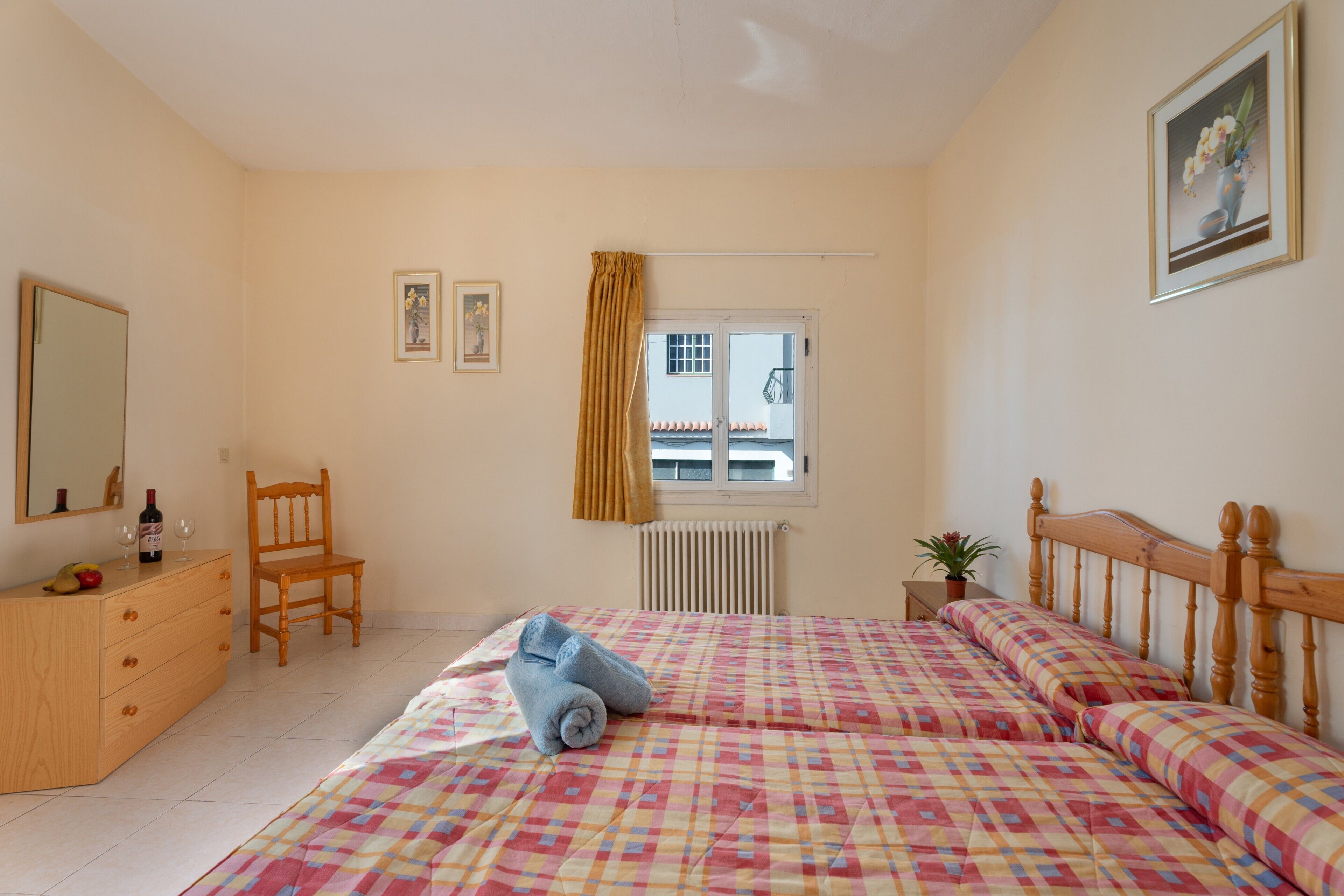 A bedroom with a bed, a wooden dresser, a chair, a window with a curtain, and a radiator.