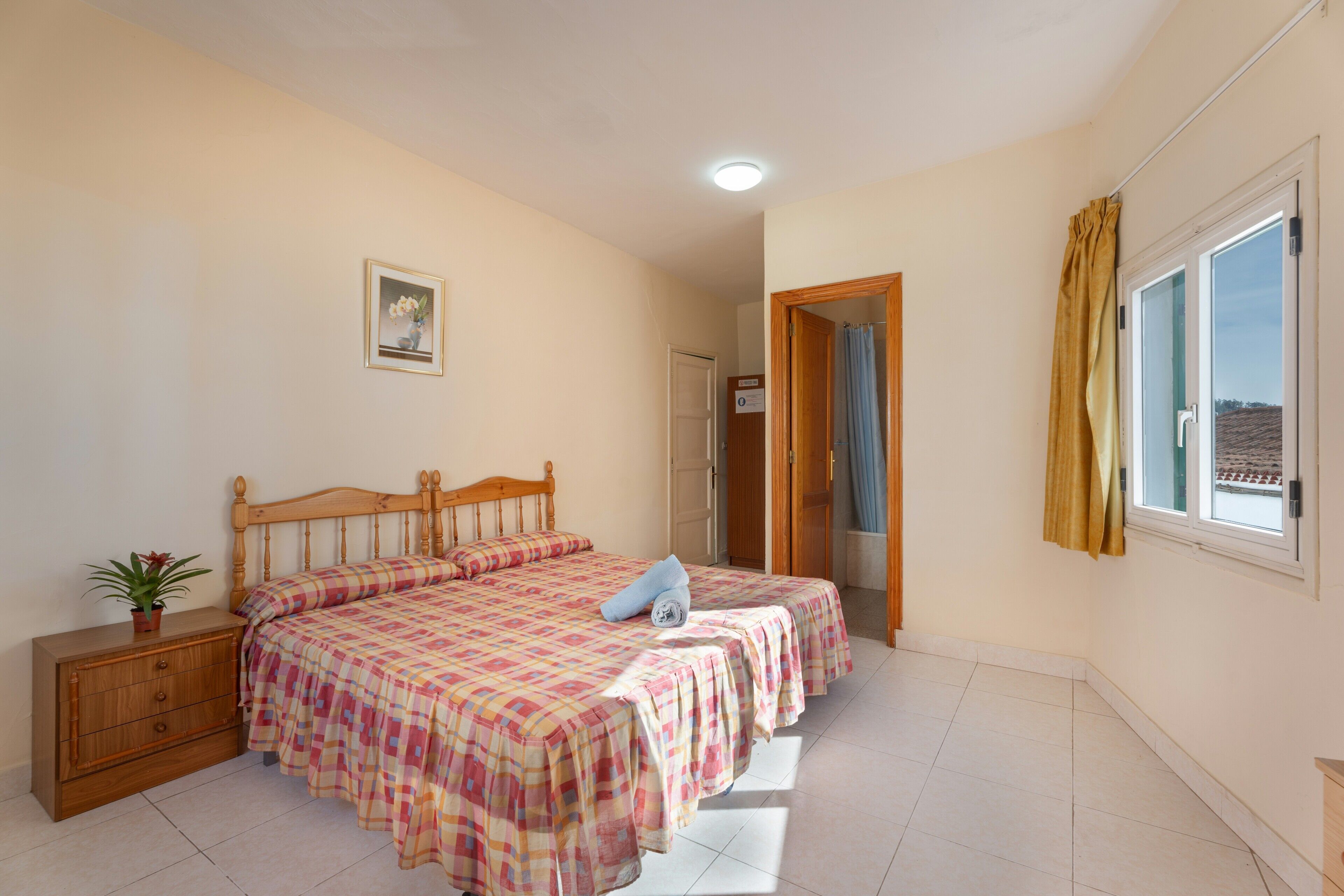 A bedroom with a bed, a dresser, a window with curtains, and a door leading to another room.