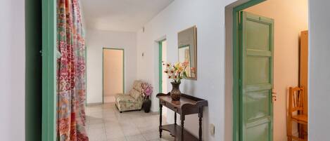A hallway with a patterned curtain, a floral vase on a console table, a chair, and a door with a green frame.