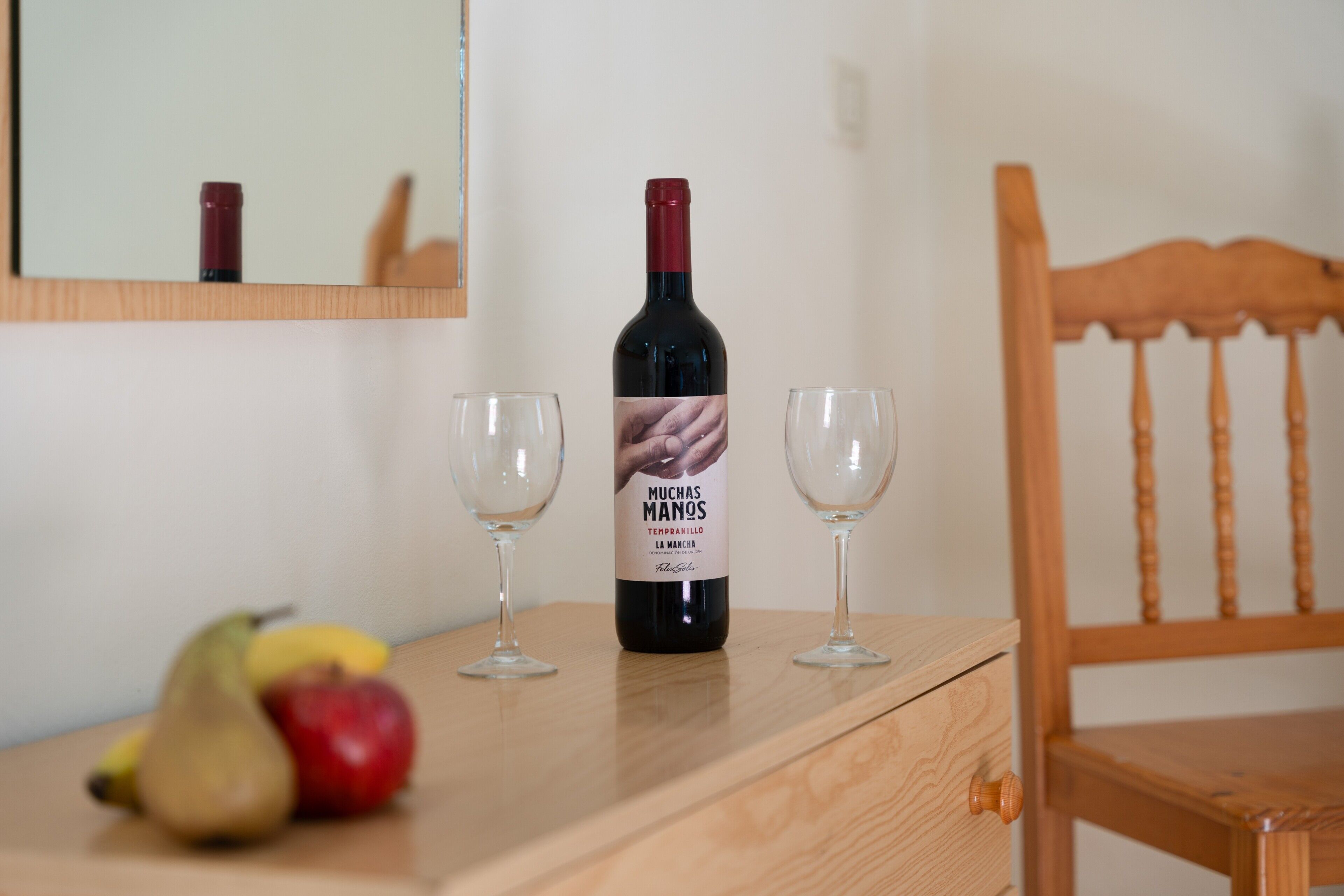 Une bouteille de vin, deux verres et une chaise en bois sur une table.