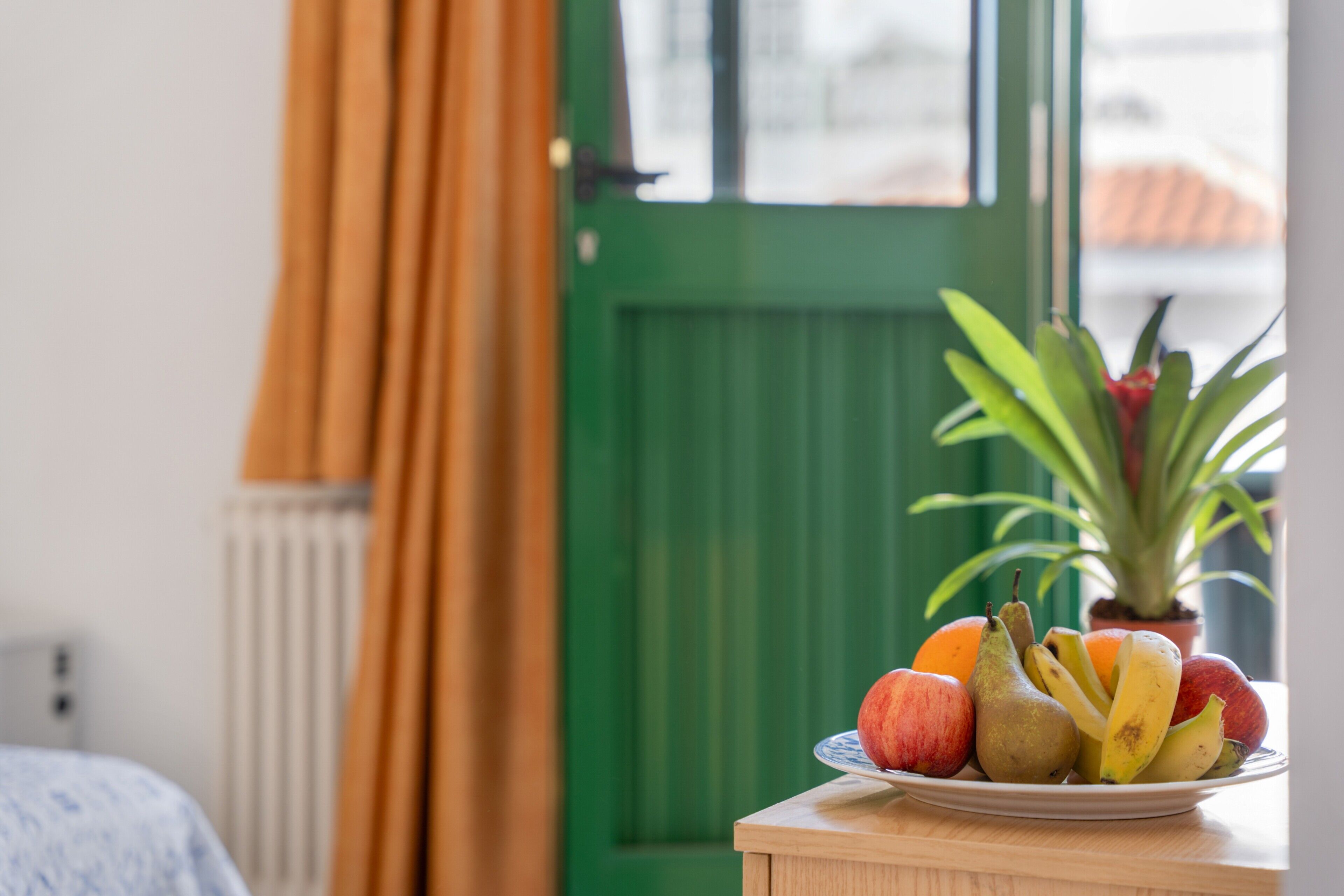 A fruit bowl on a table with a green door and curtains in the background.