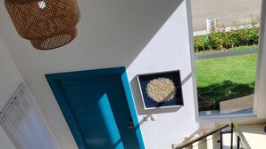 Un salon moderne avec une porte bleue, une œuvre d’art accrochée au mur, un escalier et une vue sur une pelouse verdoyante.