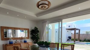 Un espace repas moderne avec une table en verre et des chaises en bois, un grand miroir au-dessus de la table et une vue sur le jardin à travers des portes vitrées.